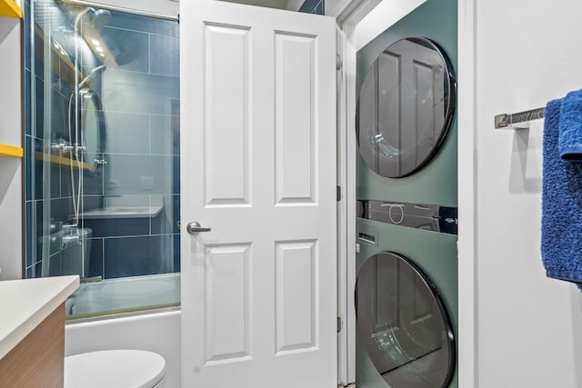 full bathroom with toilet, combined bath / shower with glass door, stacked washer / dryer, and vanity
