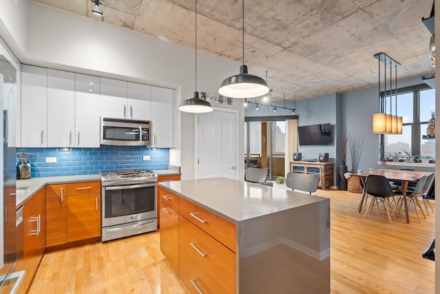 kitchen featuring appliances with stainless steel finishes, a kitchen island, backsplash, and light wood finished floors