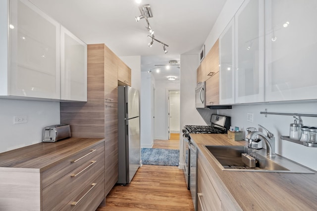 kitchen featuring appliances with stainless steel finishes, modern cabinets, a sink, light wood-style floors, and butcher block countertops