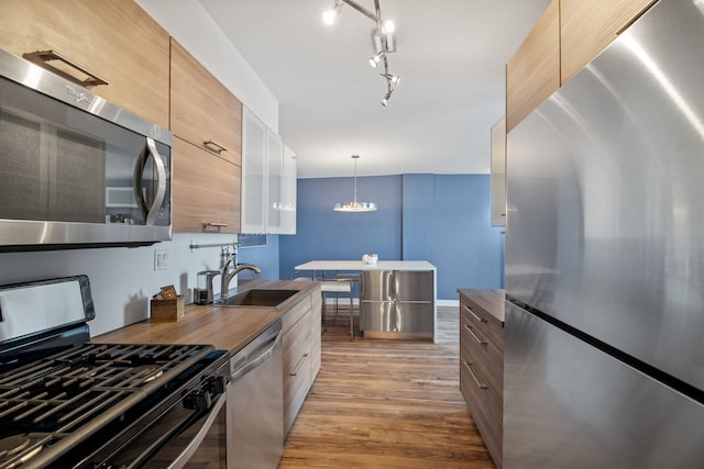 kitchen with appliances with stainless steel finishes, modern cabinets, hanging light fixtures, light wood-type flooring, and a sink