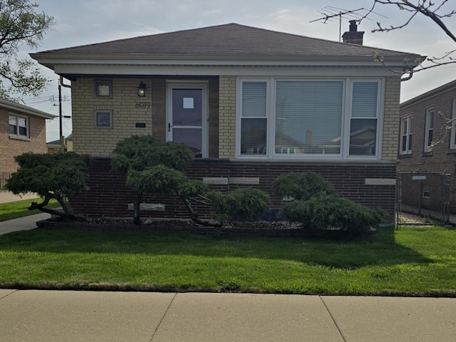bungalow-style home with a chimney, a front yard, and brick siding