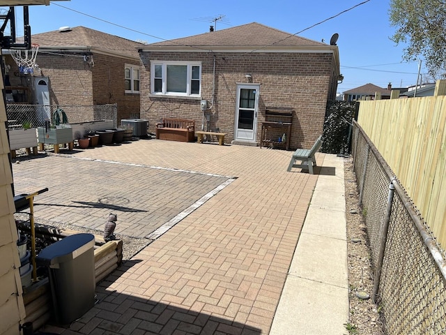 rear view of house with a patio, brick siding, a fenced backyard, cooling unit, and roof with shingles