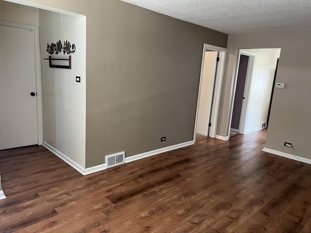 unfurnished room featuring dark wood-style flooring, visible vents, a textured ceiling, and baseboards