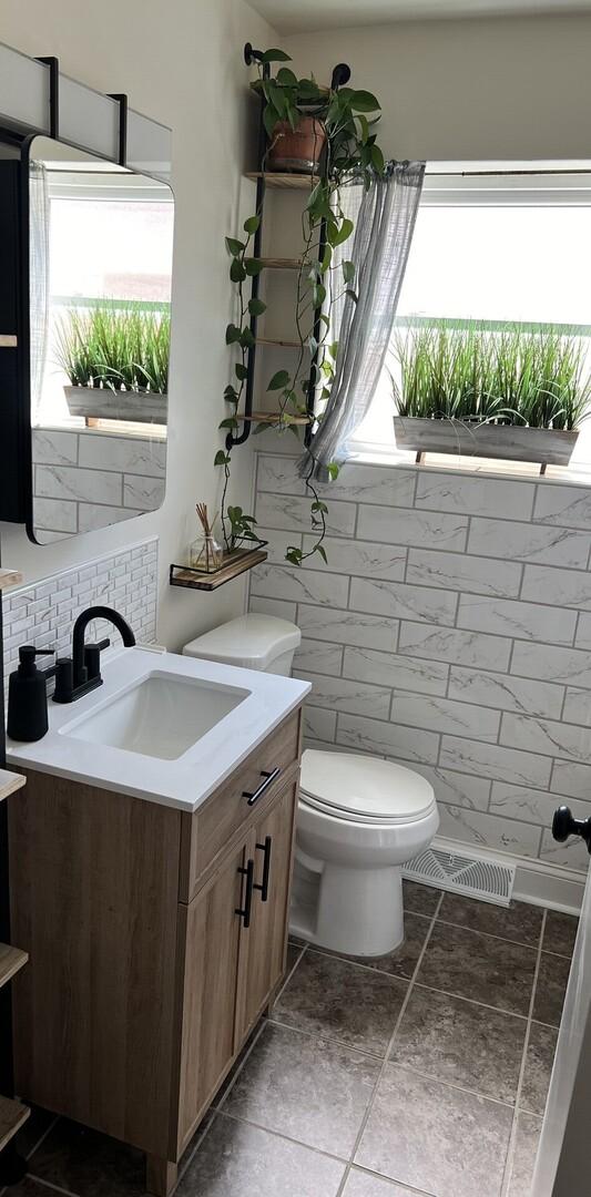 half bathroom featuring toilet, tile walls, and vanity