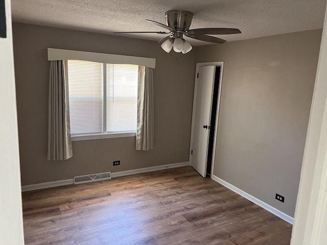 empty room featuring visible vents, wood finished floors, ceiling fan, and a textured ceiling