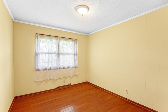 spare room with wood-type flooring, baseboards, visible vents, and ornamental molding
