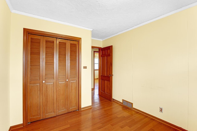 unfurnished bedroom featuring baseboards, ornamental molding, light wood-style flooring, and visible vents