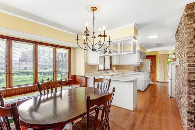 dining space with light wood-type flooring, ornamental molding, and a notable chandelier