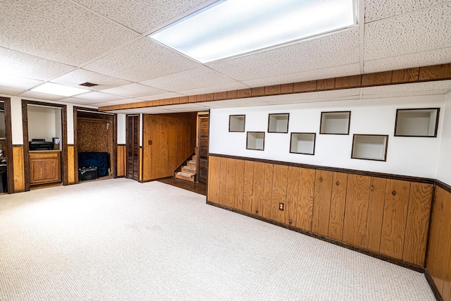 finished basement featuring stairway, carpet floors, wood walls, and a paneled ceiling