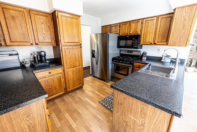 kitchen featuring stainless steel appliances, dark countertops, a sink, and light wood-style flooring
