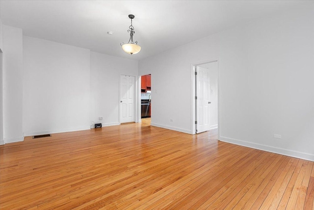 empty room featuring baseboards, light wood finished floors, and visible vents
