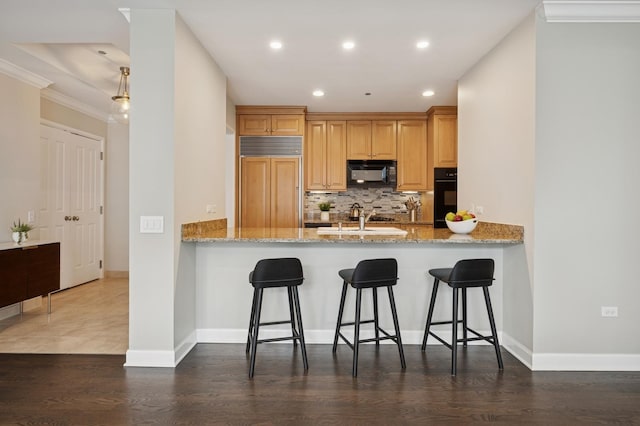 kitchen with a peninsula, light stone counters, decorative backsplash, and black appliances