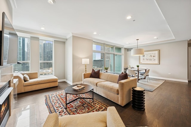 living room featuring ornamental molding, wood finished floors, baseboards, a warm lit fireplace, and recessed lighting
