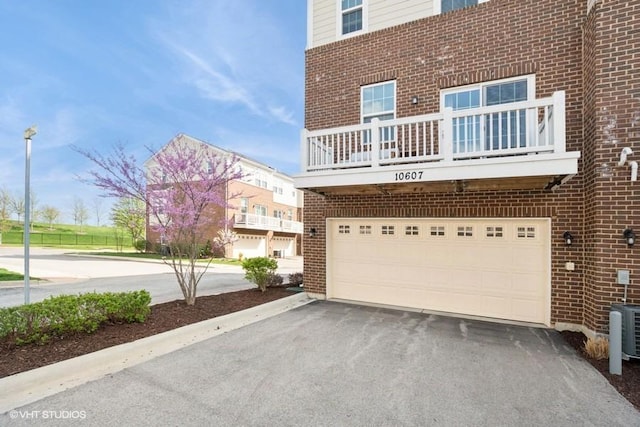 view of side of home featuring brick siding, a garage, aphalt driveway, and a balcony