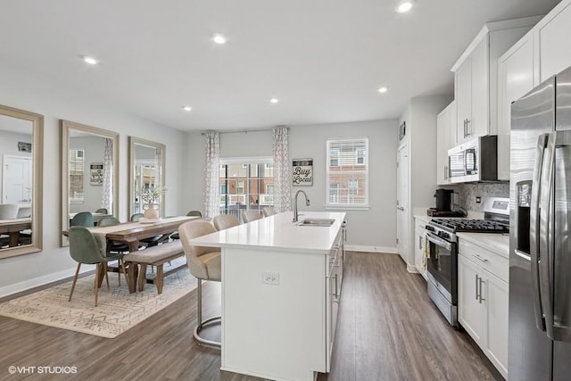 kitchen with an island with sink, a sink, dark wood-style flooring, and appliances with stainless steel finishes