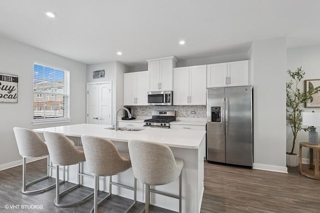 kitchen featuring a sink, appliances with stainless steel finishes, baseboards, and an island with sink