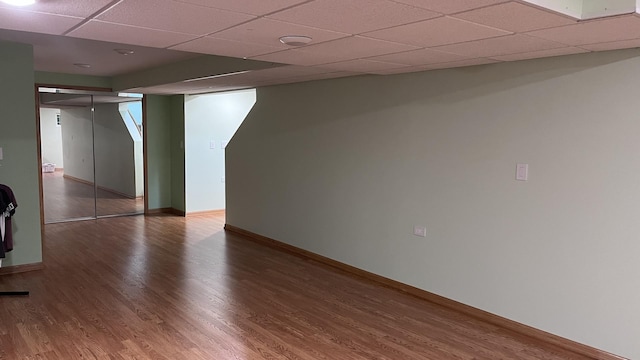 finished basement with baseboards, a drop ceiling, and wood finished floors