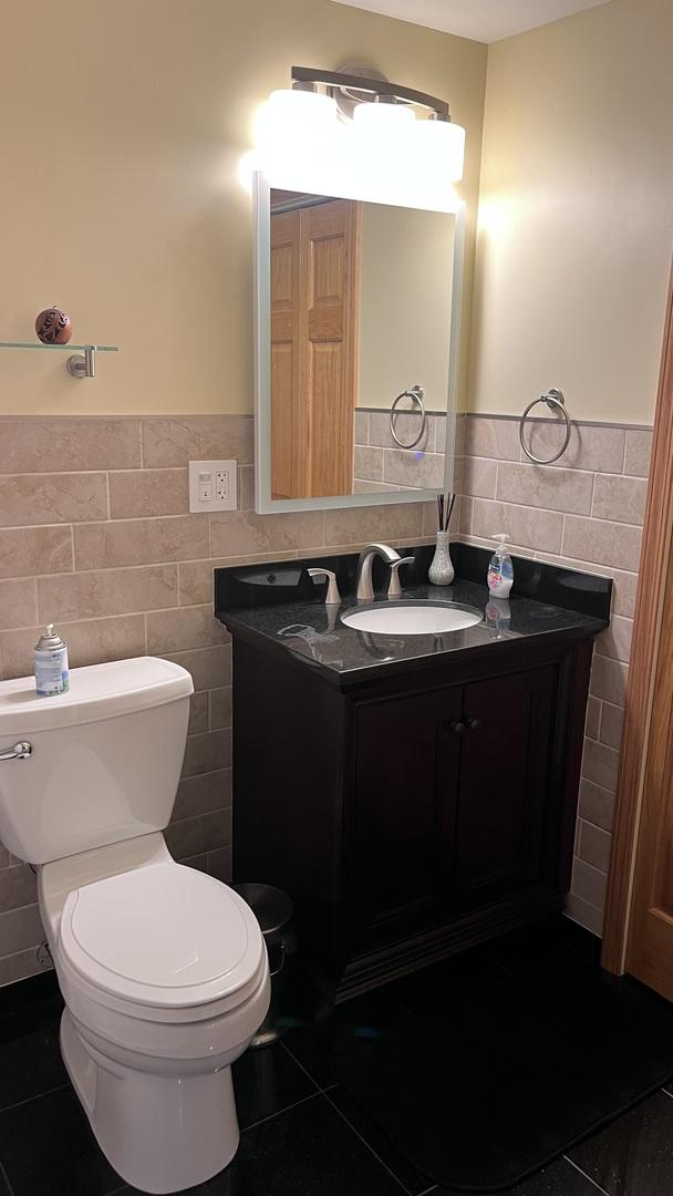 half bathroom with toilet, tile patterned floors, tile walls, and a wainscoted wall