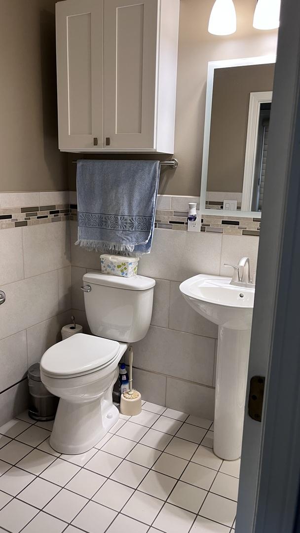 bathroom featuring toilet, tile walls, tile patterned flooring, and a wainscoted wall