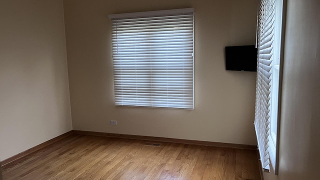 spare room featuring baseboards, wood finished floors, a wealth of natural light, and visible vents