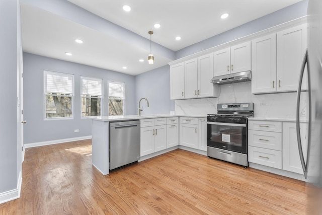 kitchen with a peninsula, white cabinets, appliances with stainless steel finishes, and under cabinet range hood