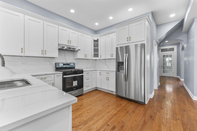 kitchen featuring a sink, under cabinet range hood, light wood-type flooring, white cabinetry, and appliances with stainless steel finishes