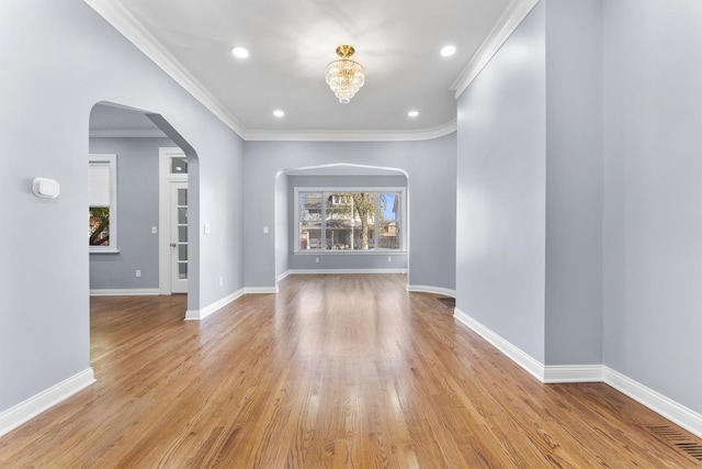 empty room featuring recessed lighting, arched walkways, light wood finished floors, baseboards, and crown molding