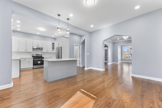kitchen featuring stainless steel appliances, under cabinet range hood, light countertops, arched walkways, and white cabinets