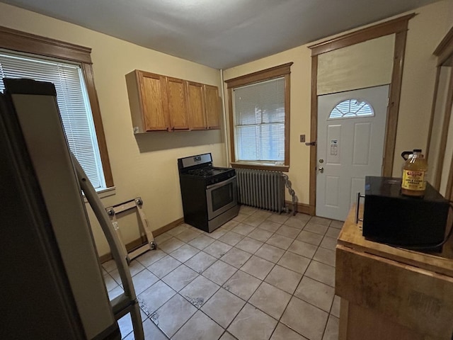 kitchen with radiator heating unit, light tile patterned floors, baseboards, and stainless steel gas stove