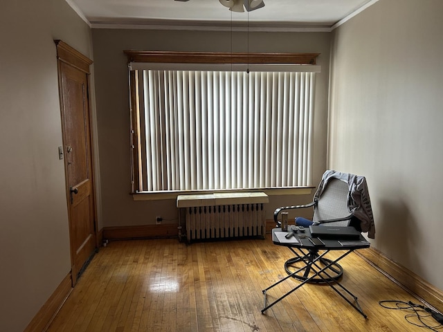 living area featuring wood-type flooring, ornamental molding, radiator, baseboards, and a ceiling fan