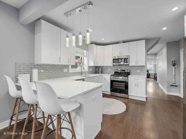 kitchen with backsplash, appliances with stainless steel finishes, a sink, white cabinets, and a peninsula