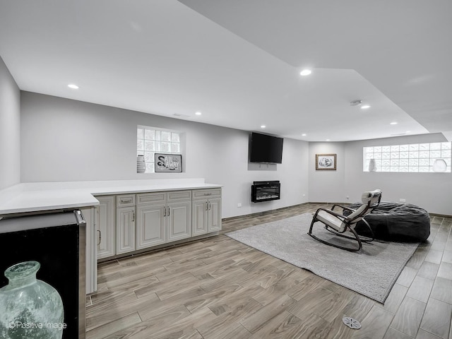 living area with a glass covered fireplace, recessed lighting, and light wood-style flooring