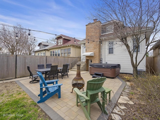 view of patio with a hot tub, a fire pit, a fenced backyard, and outdoor dining space