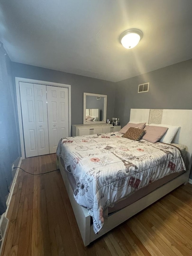 bedroom with baseboards, dark wood finished floors, visible vents, and a closet