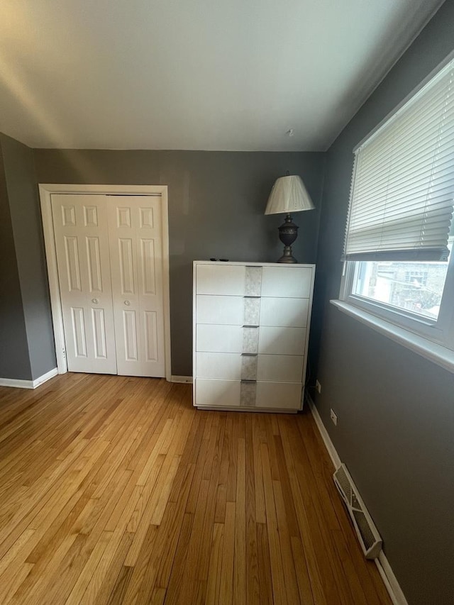 unfurnished bedroom featuring baseboards, a closet, wood finished floors, and visible vents