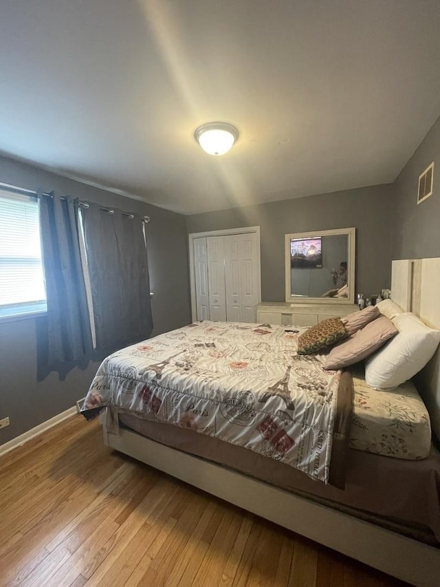 bedroom with baseboards, visible vents, hardwood / wood-style flooring, and a closet