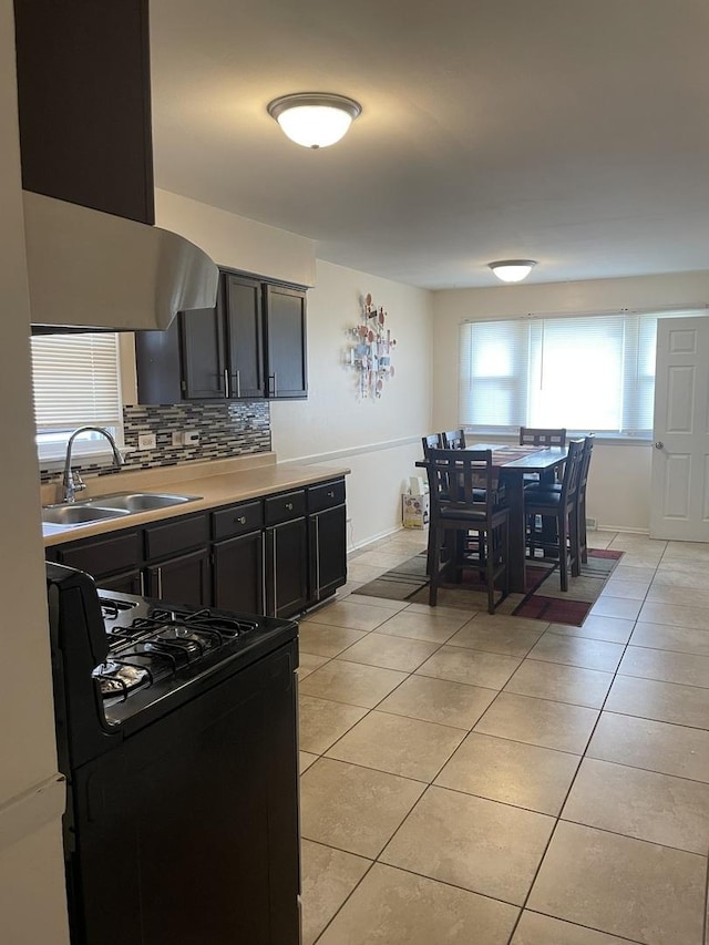 kitchen with black gas stove, range hood, dark cabinetry, a sink, and light tile patterned floors