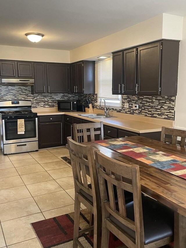 kitchen featuring black microwave, stainless steel gas stove, light tile patterned floors, tasteful backsplash, and under cabinet range hood