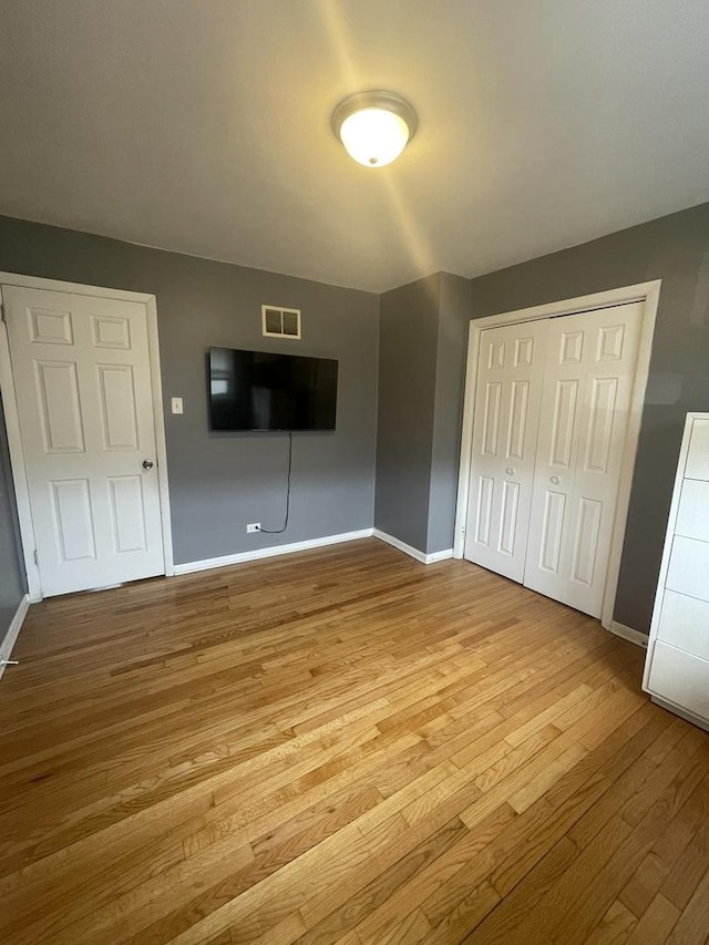 unfurnished bedroom with baseboards, wood finished floors, visible vents, and a closet