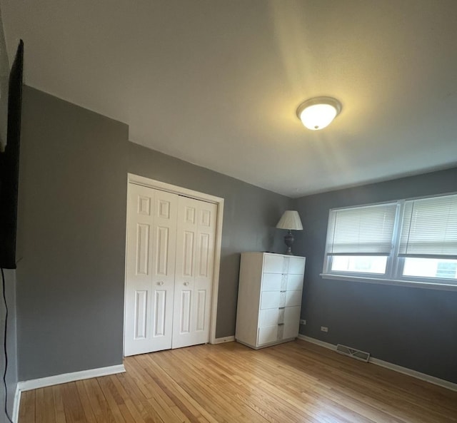 unfurnished bedroom featuring visible vents, baseboards, wood finished floors, and a closet