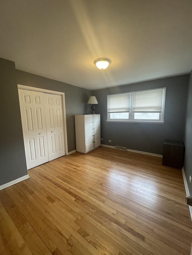 unfurnished bedroom featuring baseboards, a closet, visible vents, and hardwood / wood-style floors