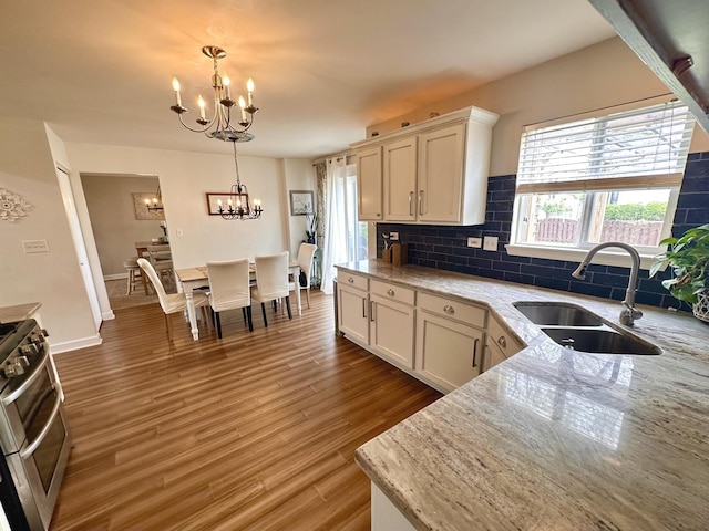 kitchen featuring tasteful backsplash, white cabinetry, a sink, an inviting chandelier, and light wood-style flooring