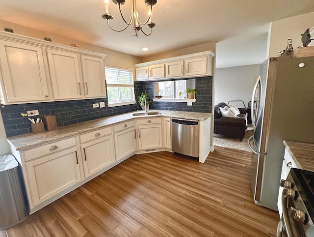 kitchen with appliances with stainless steel finishes, wood finished floors, a sink, light countertops, and a notable chandelier