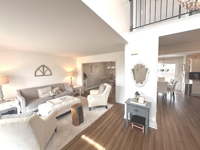 living area featuring baseboards, a high ceiling, dark wood-style flooring, and a notable chandelier