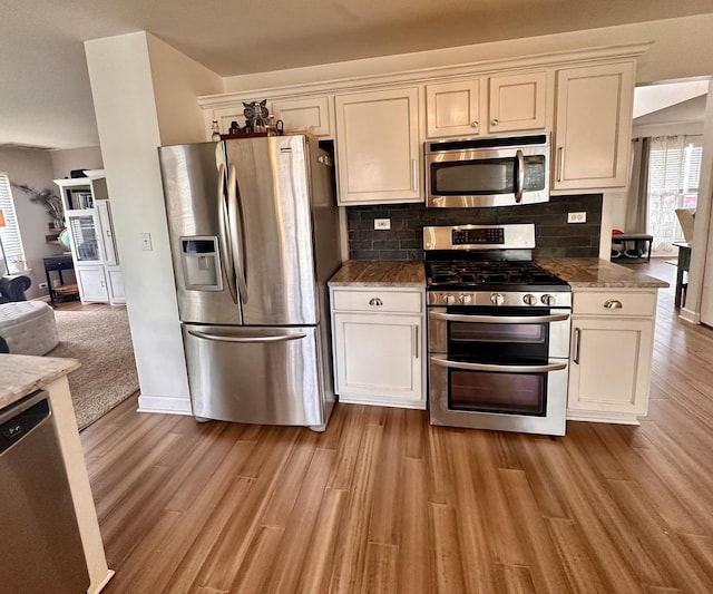kitchen featuring appliances with stainless steel finishes, light wood-style floors, open floor plan, stone counters, and backsplash