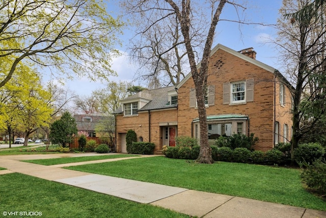 tudor house featuring brick siding, a chimney, a front yard, and a garage