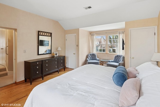 bedroom with visible vents, light wood-style floors, and vaulted ceiling