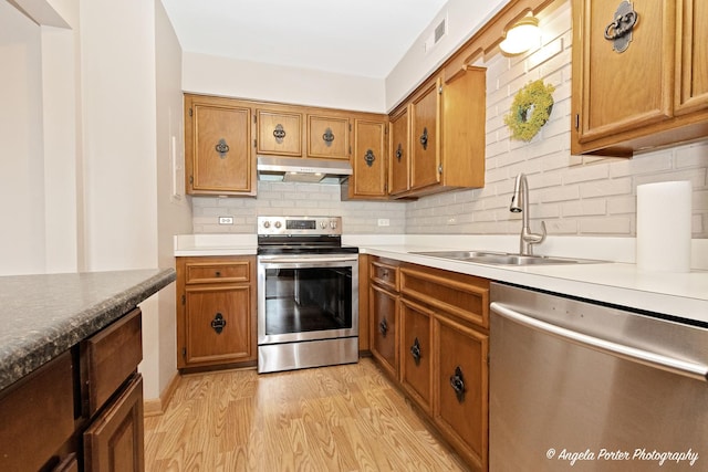 kitchen featuring visible vents, appliances with stainless steel finishes, a sink, light wood-style floors, and under cabinet range hood