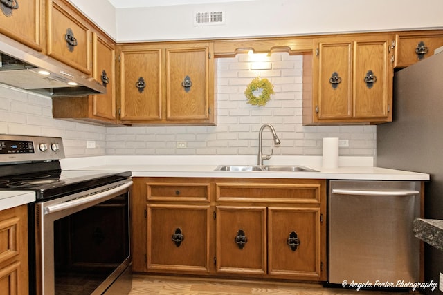 kitchen featuring a sink, decorative backsplash, stainless steel appliances, and under cabinet range hood