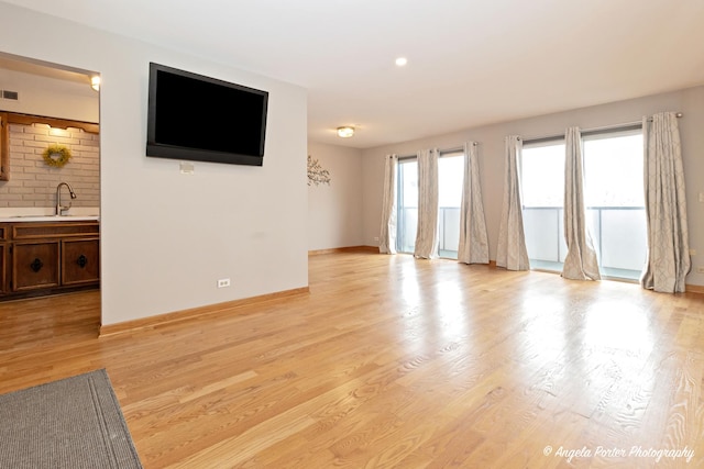 unfurnished living room featuring visible vents, a sink, light wood-style flooring, and baseboards